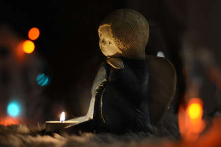A ceramic candlestick in the shape of an angel stands on the table in the Christmas lights of garlandsの写真素材