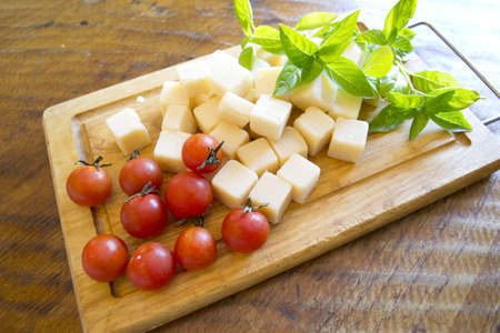 little tomatoes, parmisan cubes and basil leaves on a wooden chopping boardの写真素材