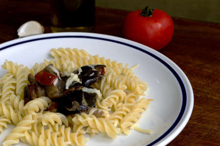 fusilli and eggplant on a wooden table with ingredients in the backgroundの写真素材