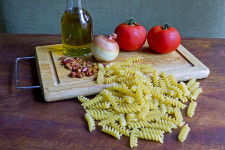 raw pasta and tomatoes, garlic, oil and peppers on a wooden chopping boardの写真素材