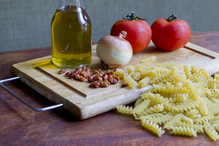 raw pasta and tomatoes, garlic, oil and peppers on a wooden chopping boardの写真素材