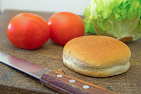 bun with knife, tomaotes nand lettuce on a cutting boardの写真素材