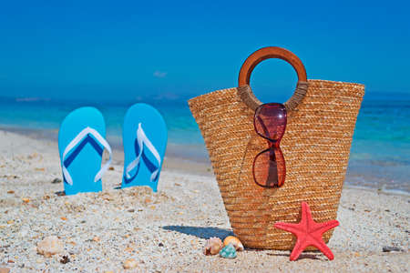 straw bag by the shore with blue sandals on the backgroundの写真素材