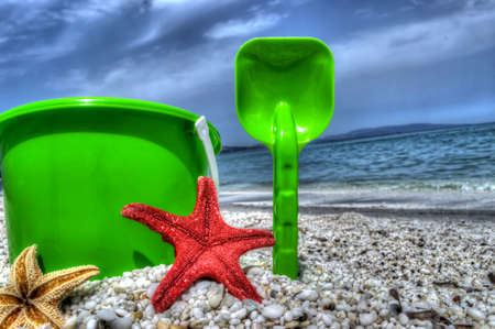 shovel, bucket and starfish on a pebbled shoreの写真素材