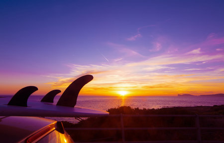 car with surfboard by the shore at sunset. Shot in Alghero, Capo Caccia in the background. Sardinia, Italyの写真素材