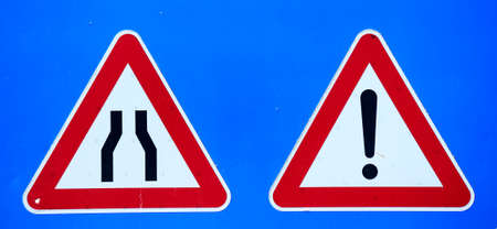 narrow road and exclamation mark signs on blue backgroundの写真素材