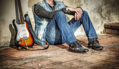 man and electric guitar leaning against a grunge wallの写真素材