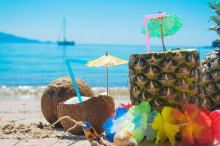 coconuts and pineapples on the sand by the seaの写真素材