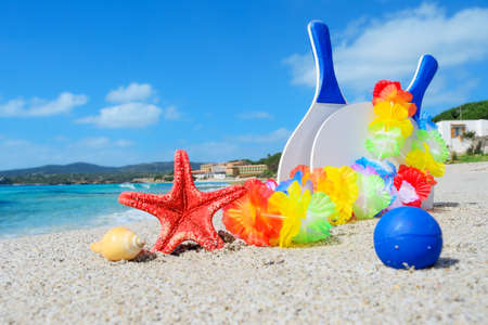 beach rackets, necklace and starfish by the shoreの写真素材