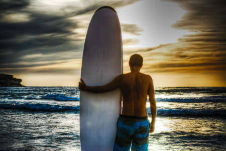 surfer and surfboard on the beach at sunsetの写真素材