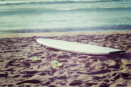 surfboard and flip flops on the sand in vintage tone