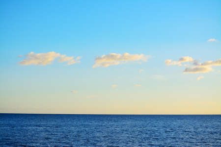 blue sea under a clear sky with small clouds at sunsetの写真素材