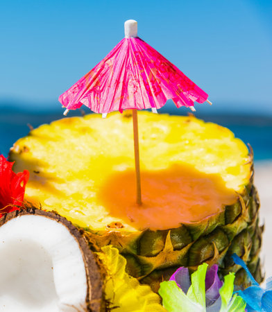 Cocktail umbrella on a pineapple half on the beach in summerの写真素材