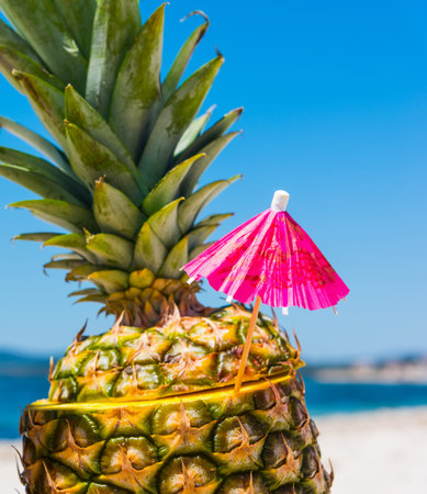 Pineapple with cocktail umbrella on the beachの写真素材