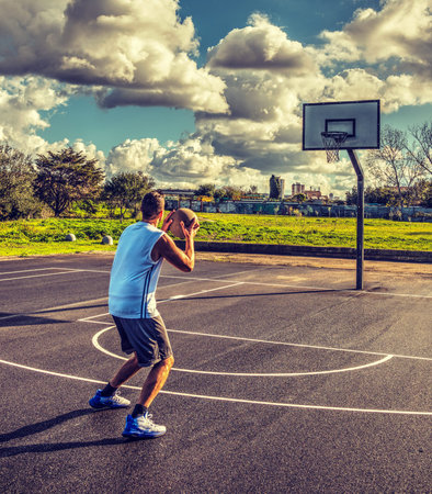 Lefty basketball player seen from behind loading a three point shot 