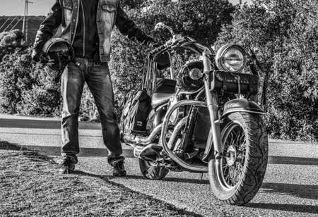 Biker standing by a classic motorcycle in black and whiteの写真素材