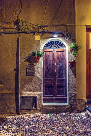 Wooden door in a rustic wall in old town Alghero by night, Italyの写真素材