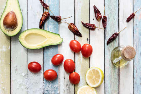 Tomatoes, avocado, chili peppers, lemon, salt and olive oil on a wooden table seen from aboveの写真素材