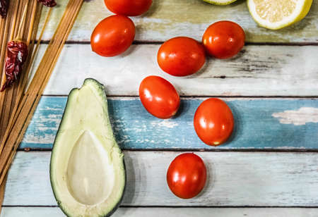 Tomatoes, avocado, spaghetti, lemon and chili peppers on a wooden table seen from aboveの写真素材