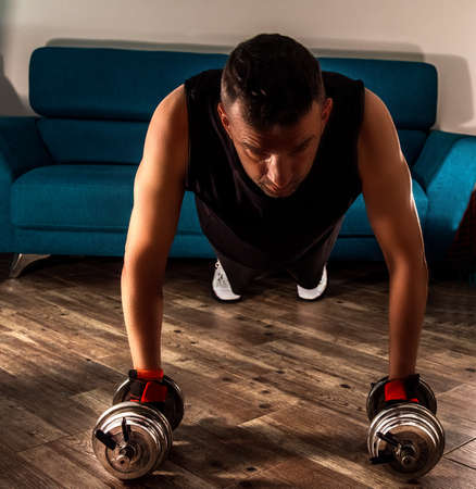 Front view of a man doing plank with dumbbells in the living room during home workoutの写真素材