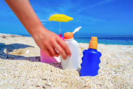Girl holding a suntan bottle on a white sand in the summerの写真素材
