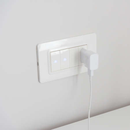 Close up of a white smartphone charger plugged in a wall socketの写真素材