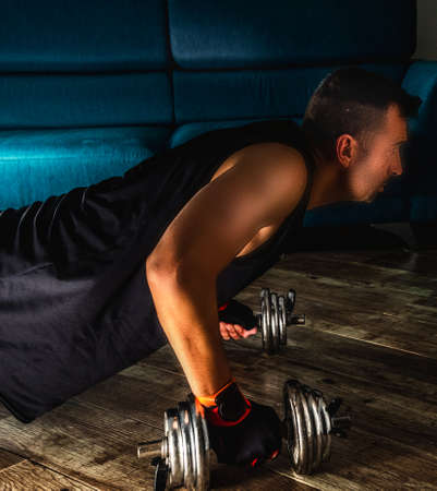 Side view of a man doing plank with metal dumbbells during home workoutの写真素材