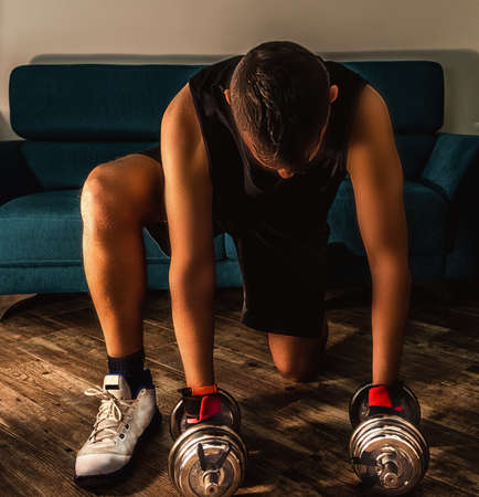 Front view of a man picking up two metal dumbbells during home workoutの写真素材
