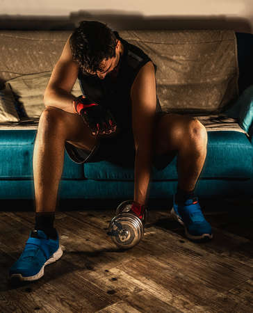 Man with a metal dumbbell doing home workout sitting on a couchの写真素材