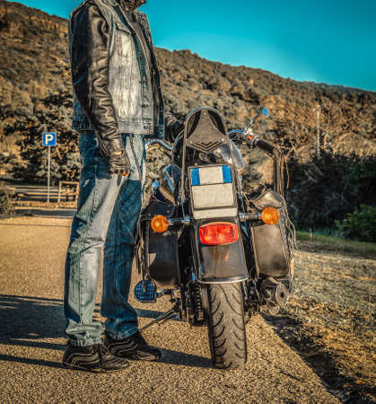 Biker standing by his motorcycle on the edge of a country road at sunsetの写真素材