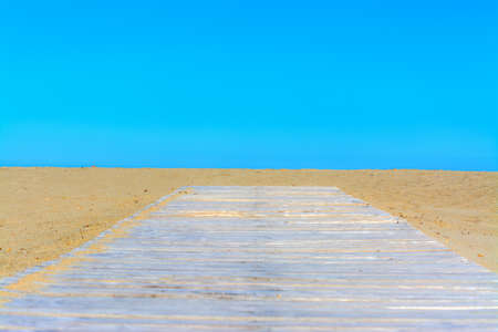 Wooden boardwalk on the beach under a blue sky in Sardinia, Italyの写真素材
