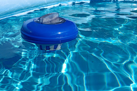 Blue chlorine dispenser floating on a swimming pool on a sunny day. Chlorine dispensers are used to...