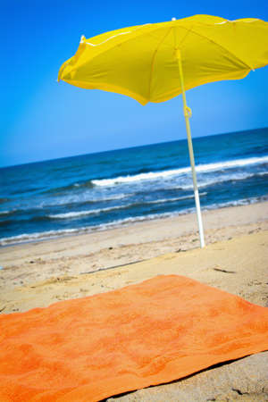 Orange towel and yellow parasol on the beach in summertimeの写真素材