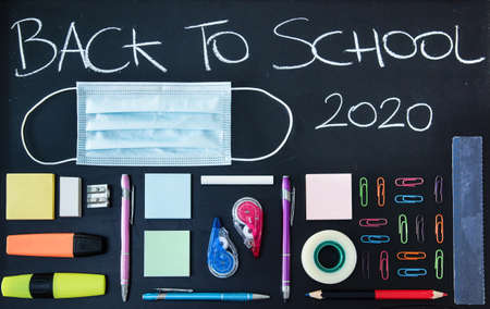 Back to School 2020 written on a chalkboard with virus protection mask and colorful school objectsの写真素材