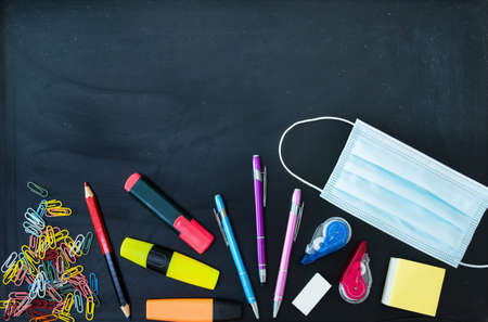 School objects and virus protective mask on a dark chalkboard seen from aboveの写真素材