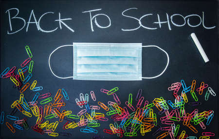 Back to school written on a chalkboard with a virus protective mask and colorful paperclipsの写真素材