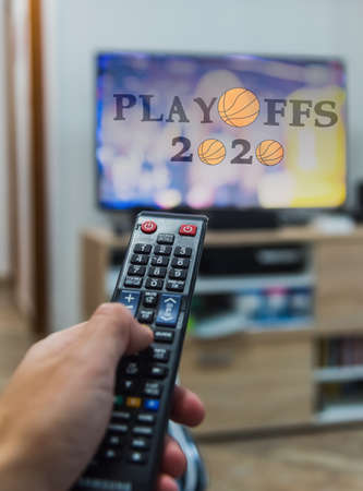 Man holding a remote control while watching basketball Playoffs 2020 on tvの写真素材
