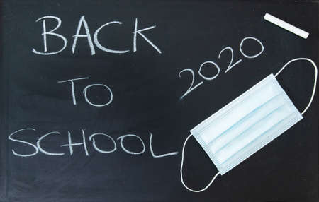 Back to school written on a dark chalkboard with a virus protective maskの写真素材