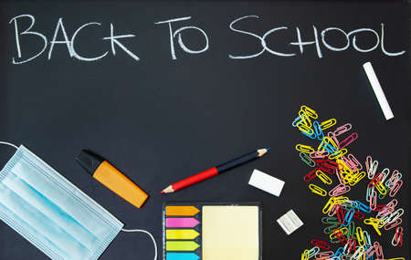 Back to school written on a black chalkboard with colorful objects and virus protective maskの写真素材