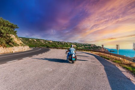 Biker on a winding road under a pink sky at sunsetの写真素材