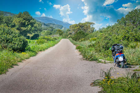 Scooter parked on the edge of a country road under a cloudy skyの写真素材