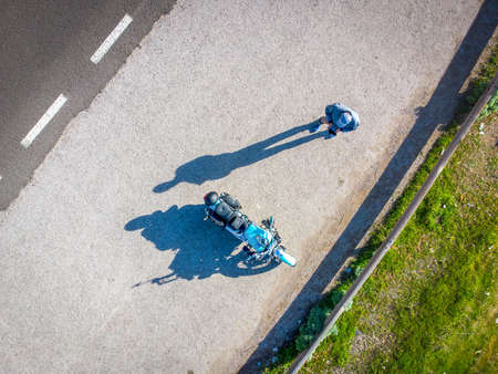 Man by a classic motorcycle on a sunny day seen from aboveの写真素材