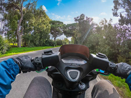 First person view of a man on a scooter riding on a country road surrounded by pine treesの写真素材