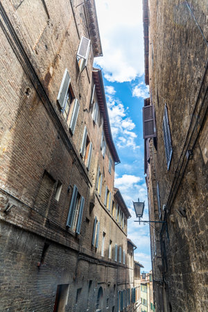 Narrow street in Siena under a blue sky with clouds. Tuscany, Italyの写真素材