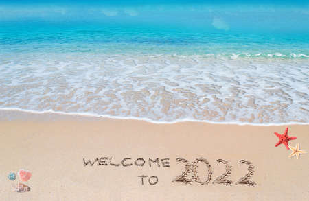 turquoise water and golden sand with shells and sea stars with "welcome to 2022" written on itの写真素材