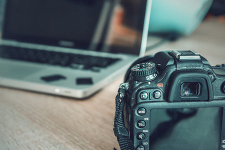 Close up of a Dslr camera on a wooden desk with a laptop on the background