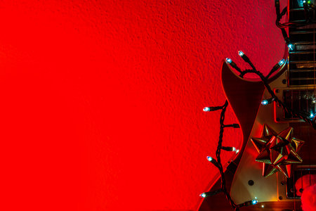 Electric guitar with Christmas lights and ribbon on a red backgroundの写真素材