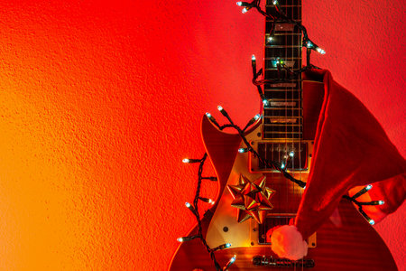 Electric guitar with Christmas lights, ribbon and Santa hat on a red and orange backgroundの写真素材