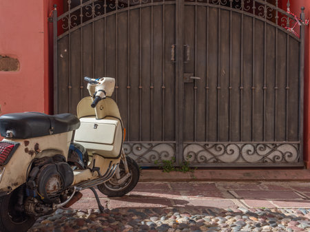 Old scooter parked by a metal gate in Sardinia, Italyの写真素材