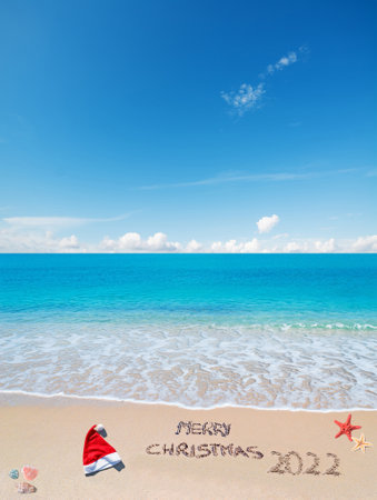 santa hat and"merry christmas 2022" written on a tropical beach under a blue skyの写真素材